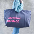 Grey oversized tote bag with neon pink text ‘emotional baggage’, displayed against a neutral background.