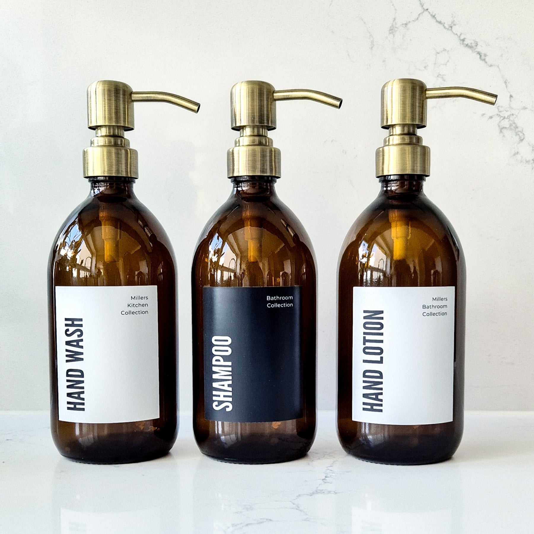 Three brown bottles with gold pumps labeled 'Hand Wash', 'Shampoo', and 'Hand Lotion' on a marble surface.