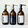 Three brown bottles labeled 'Hand Lotion', 'Shampoo', and 'Hand Wash' on a marble surface.