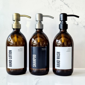 Three brown bottles labeled 'Hand Lotion', 'Shampoo', and 'Hand Wash' on a marble surface.
