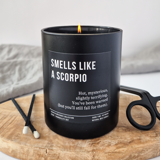 Black candle labeled 'Smells Like a Scorpio' on a wooden tray with a white background