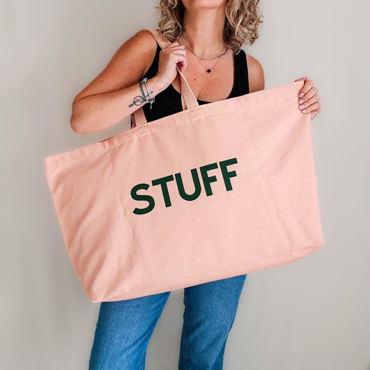 Person holding a pink tote bag with 'STUFF' printed on it against a plain background