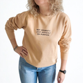 Person wearing a beige sweatshirt with text  'Not dramatic just difficult on purpose' and blue jeans on a white background