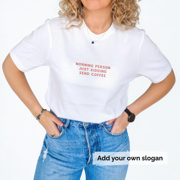 Person wearing a white t-shirt with a humorous slogan 'Morning person just kidding send coffee' and blue jeans on a plain background