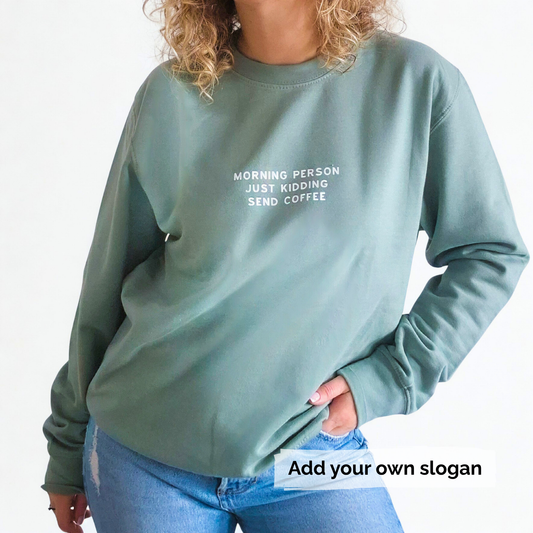 Person wearing a green sweatshirt with text 'Morning person just kidding send coffee' and jeans on a light grey background