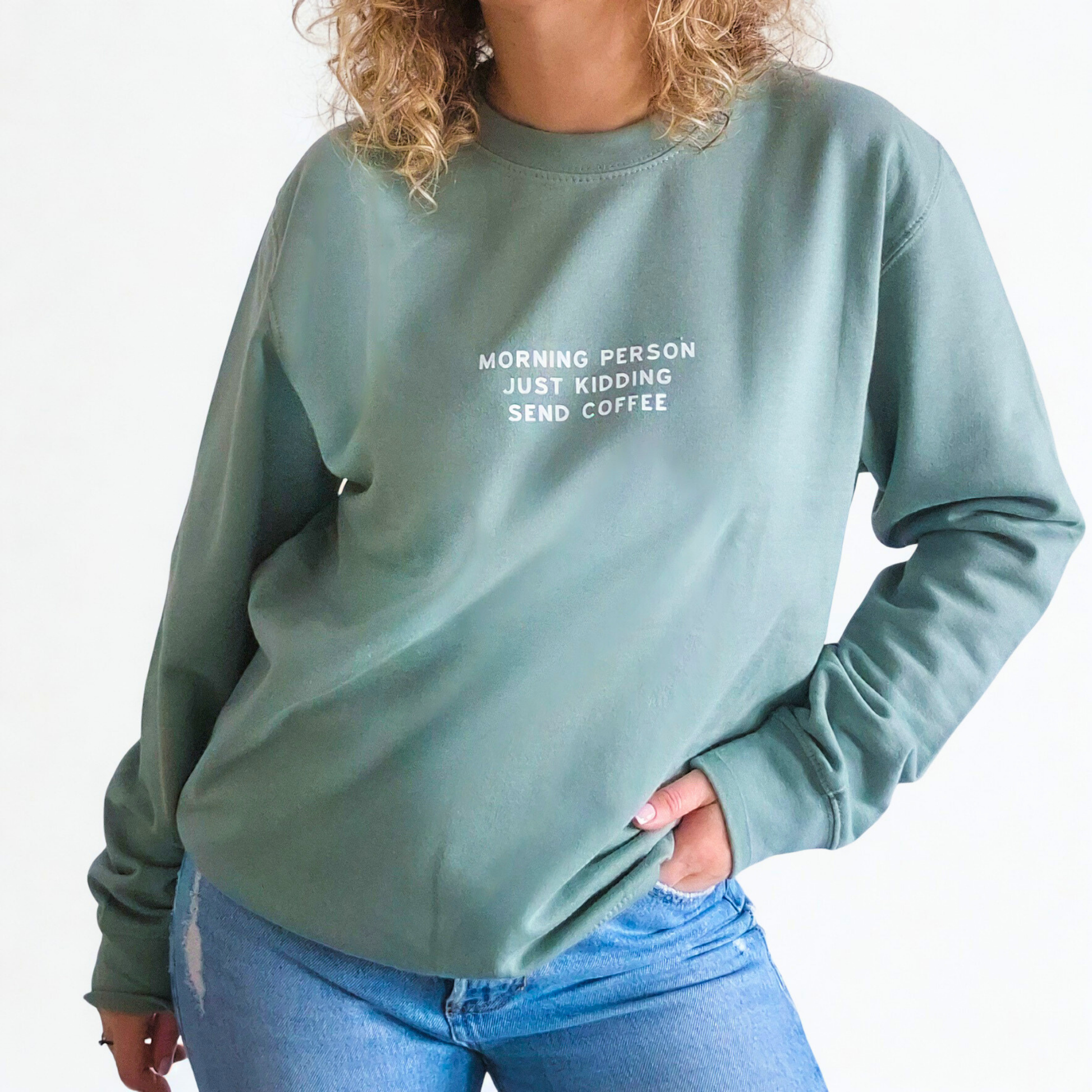 Person wearing a green sweatshirt with text 'Morning person just kidding send coffee, standing against a plain background