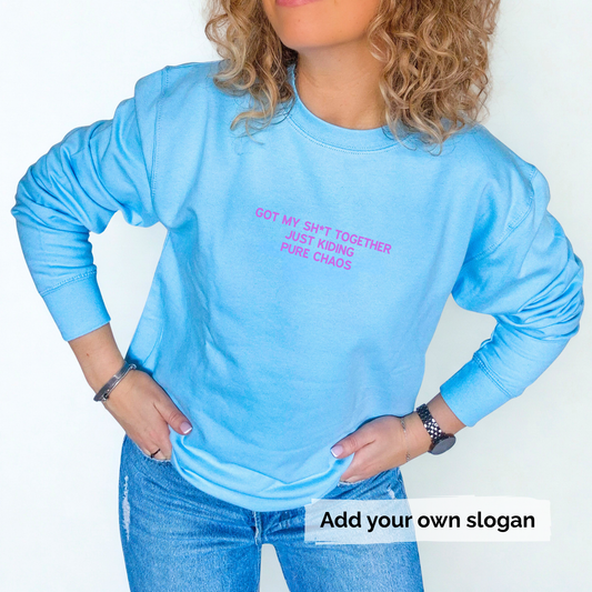 Person wearing a blue long-sleeve sweatshirt with text 'Got my shit together just kidding pure chaos' , standing against a plain background.