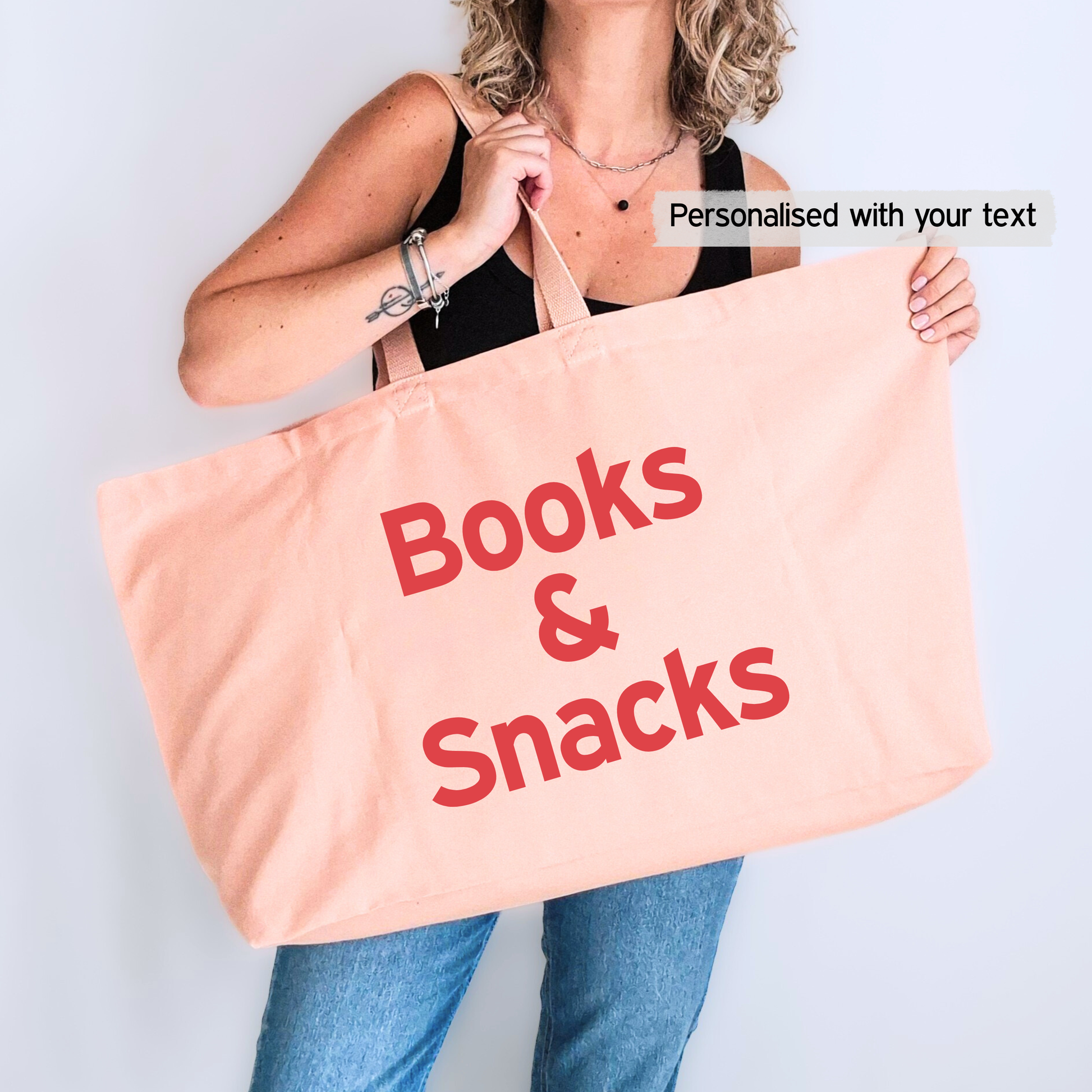 Person holding a pink tote bag with 'Books & Snacks' text on a light gray background