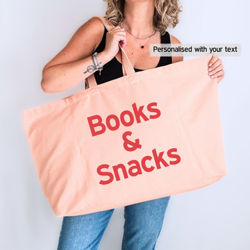 Person holding a pink tote bag with 'Books & Snacks' text on a light gray background