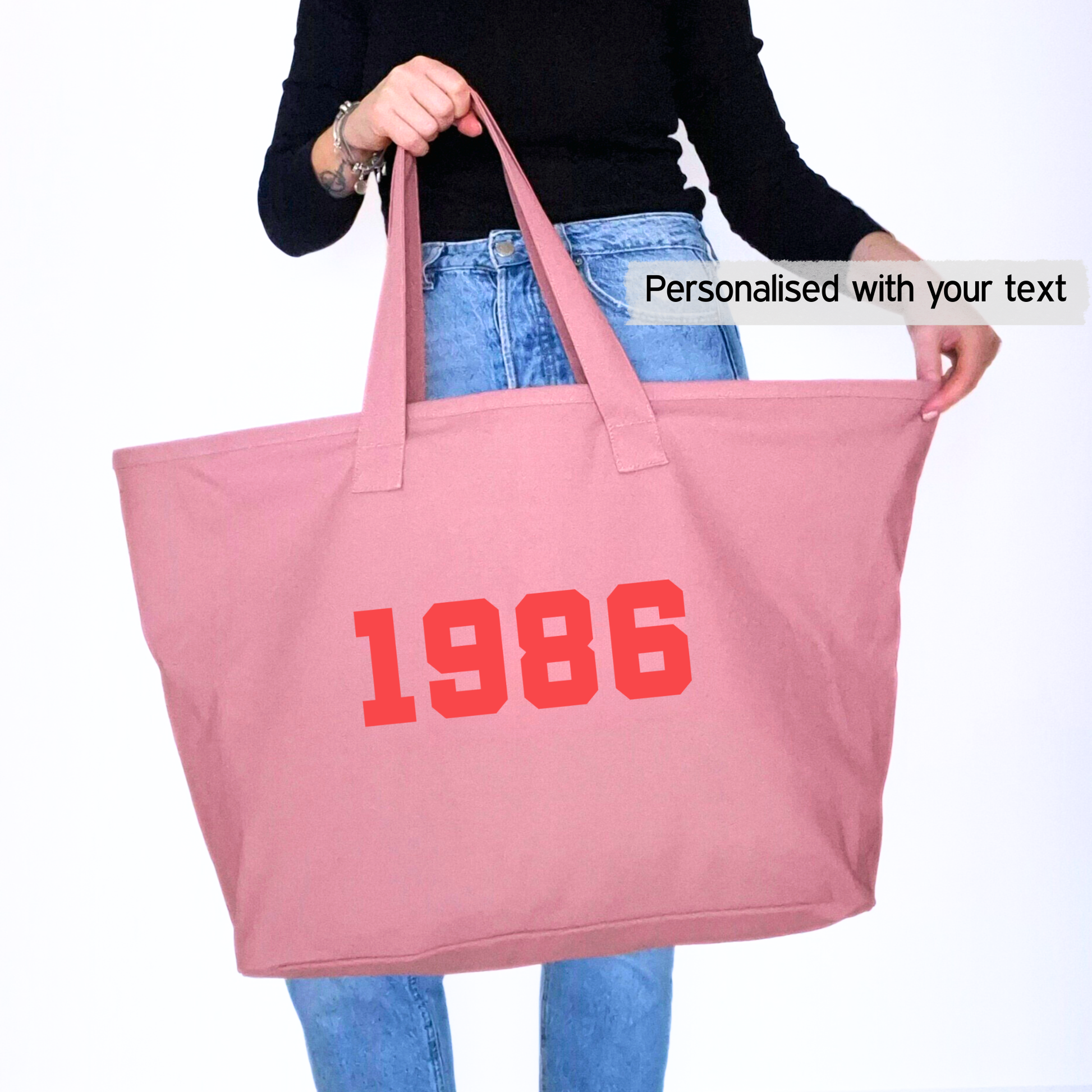 Pink tote bag with custom birth year '1986' printed on it, held by a person wearing a black top and blue jeans.