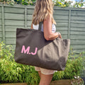 Person holding a brown tote bag with 'M.J.' initials in pink letters outdoors.