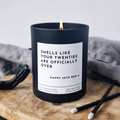 Black candle with a humorous label 'Smells like your  twenties are officially over' on a wooden surface