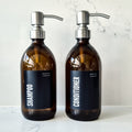 Two brown bottles labeled 'Shampoo' and 'Conditioner' on a marble surface.