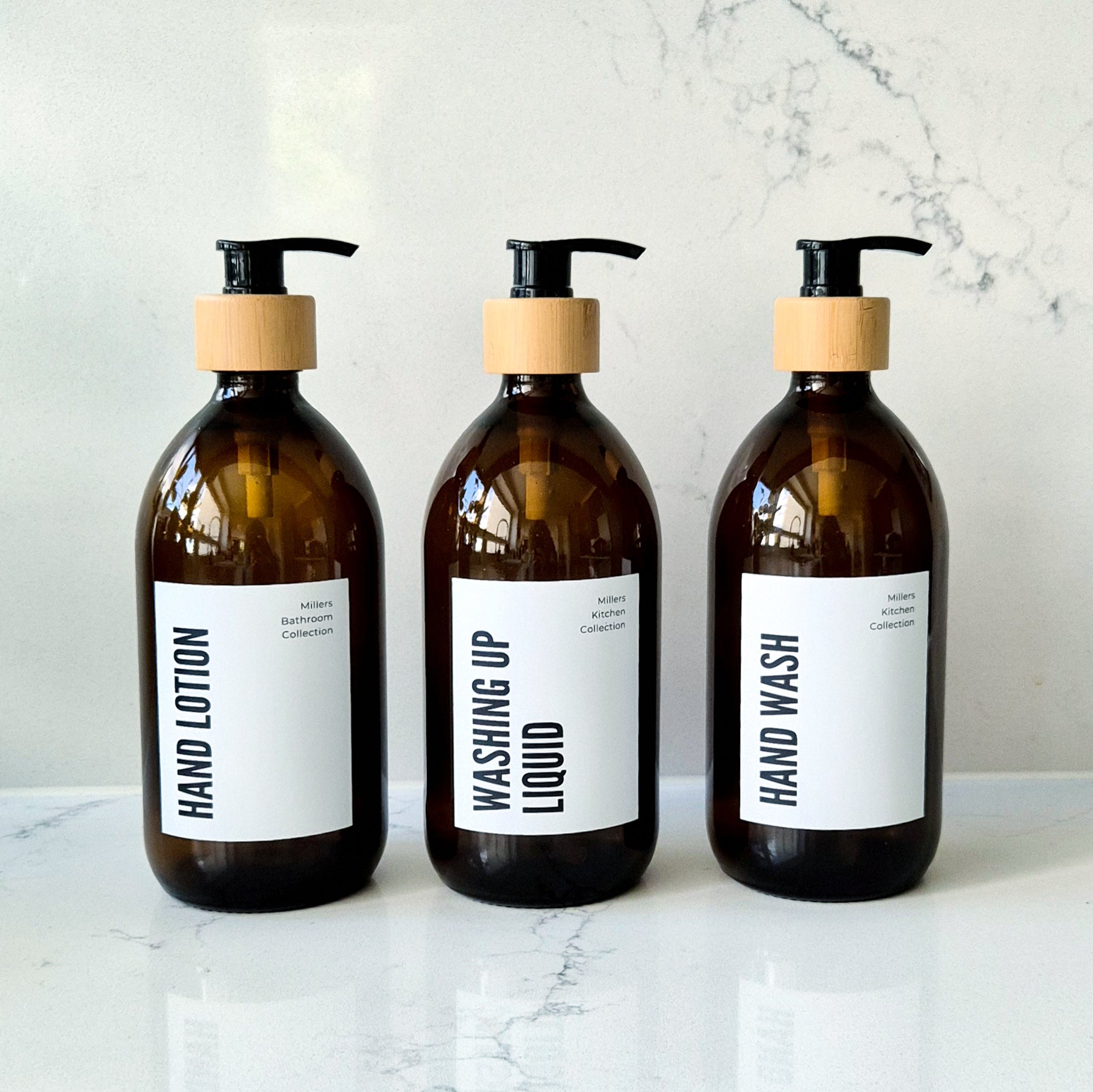 Three brown glass bottles with pump dispensers labeled 'Hand Lotion', 'Washing Up Liquid', and 'Hand Wash' on a marble surface.