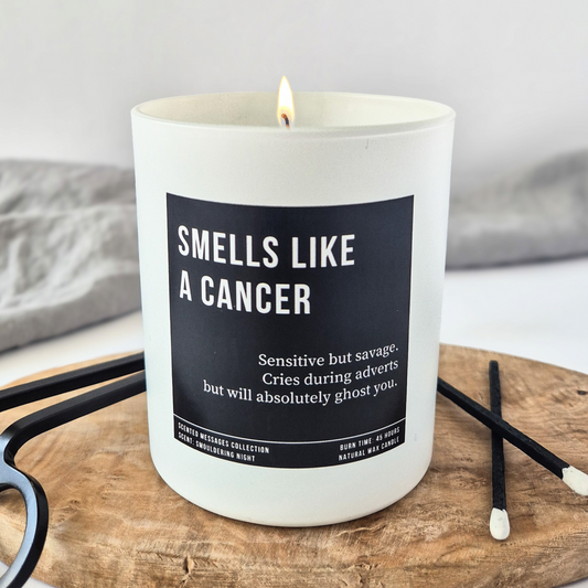 White candle with “Smells Like a Cancer” label and personalised traits below, styled with black matches and clean, minimalist background.