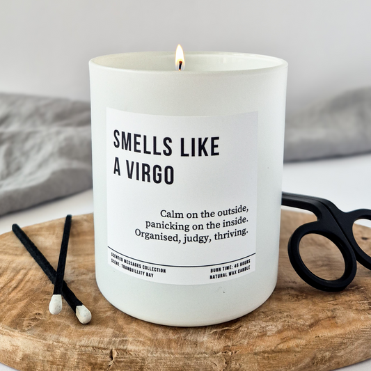 White candle with personalised 'Smells like a Virgo' text on a wooden board with black scissors and hair ties.