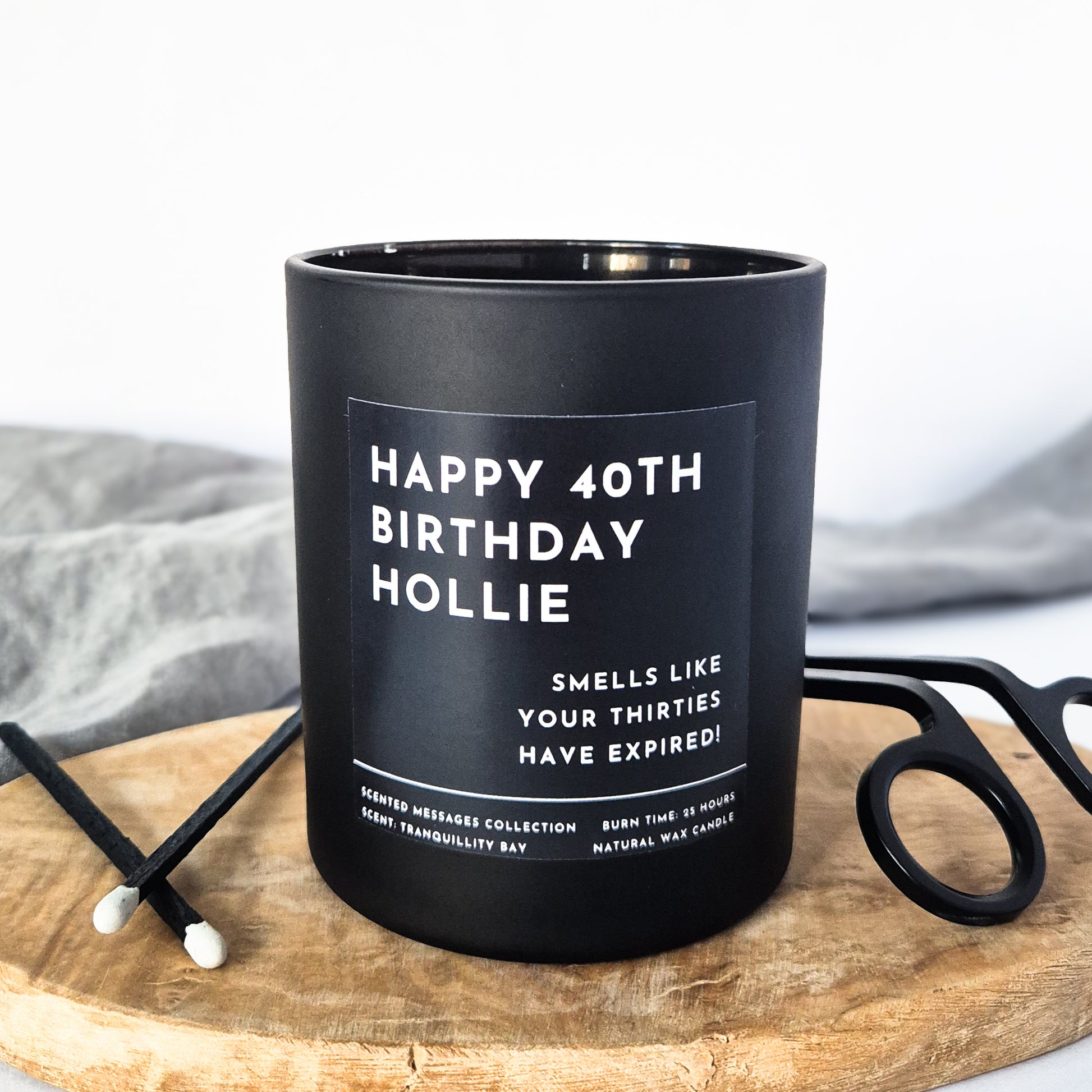 Black candle with personalised text on a wooden board with a white background