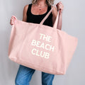 Oversized pale pink tote bag with customisable slogan ‘The Beach Club’, held in hand.