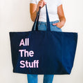 Large navy personalised tote bag with pink bold text reading All The Stuff, held in hand.