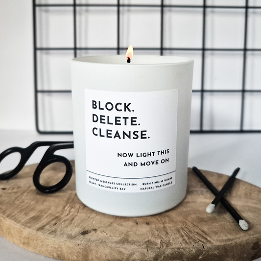 Candle with a humorous post break up  message 'Block. Delete. Cleanse. Now light this and move on' on a wooden surface