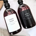 Refillable soap dispensers with white label 'Hand soap' and a family name underneath and a black label 'body wash' and a personalised address