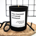 Black candle with a humorous label 'You finished an Ironman' on a wooden surface 