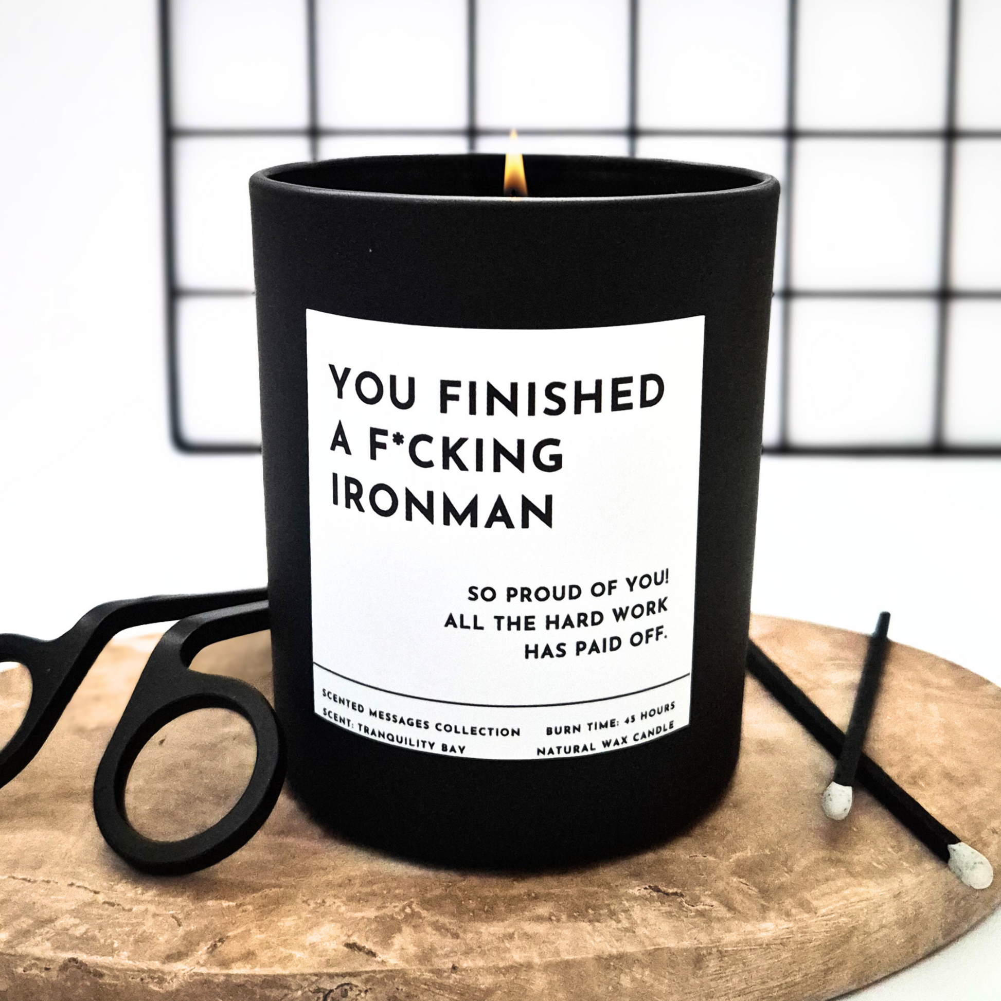 Black candle with a humorous label 'You finished an Ironman' on a wooden surface 