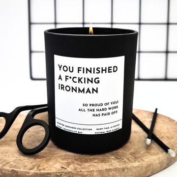 Black candle with a humorous label 'You finished an Ironman' on a wooden surface 