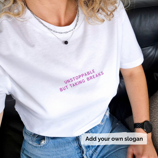 Person wearing a white t-shirt with pink text 'Unstoppable but taking breaks' and jeans, sitting on a black leather couch.