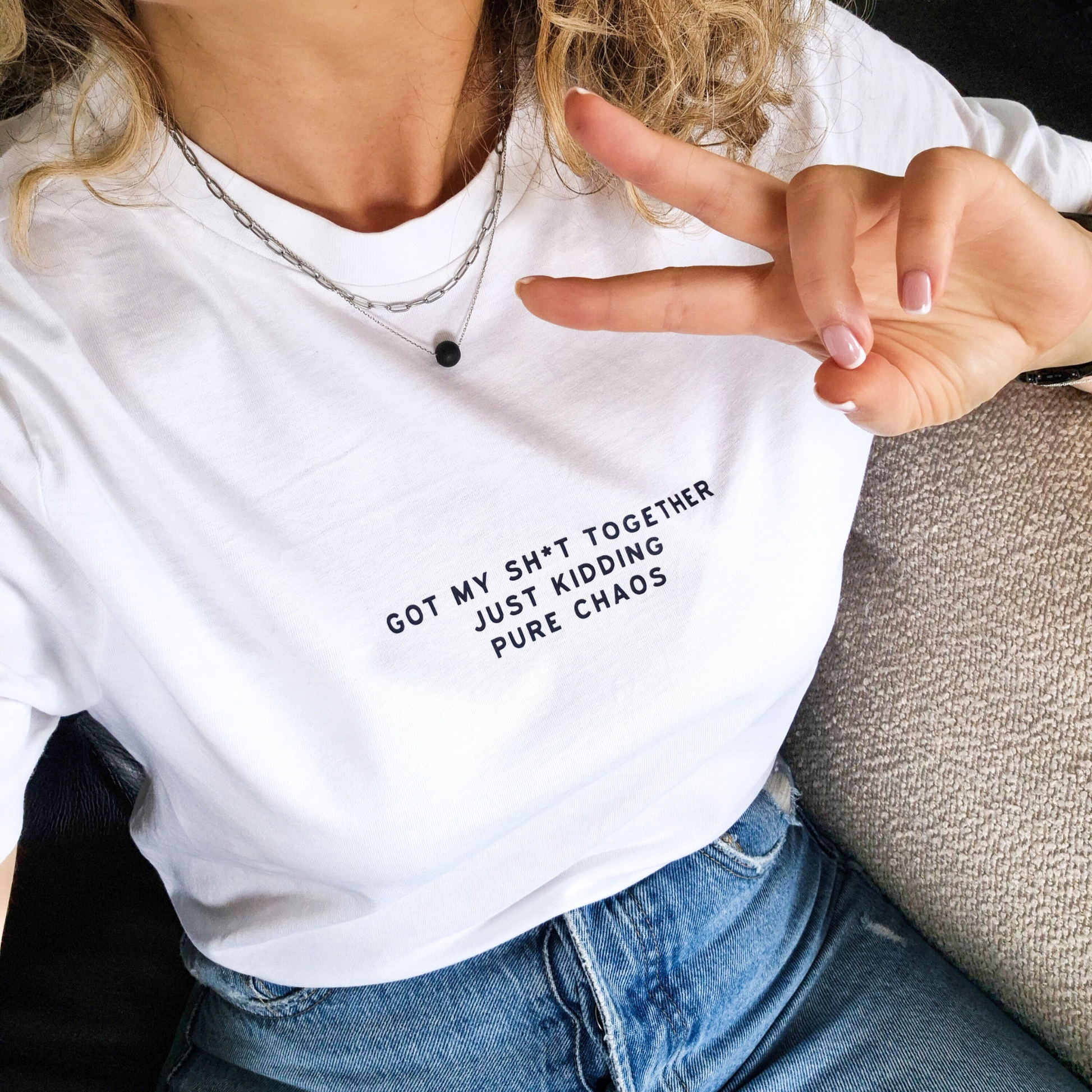 Person wearing a white t-shirt with text 'Got my shit together just kidding pure chaos' and making a peace sign.