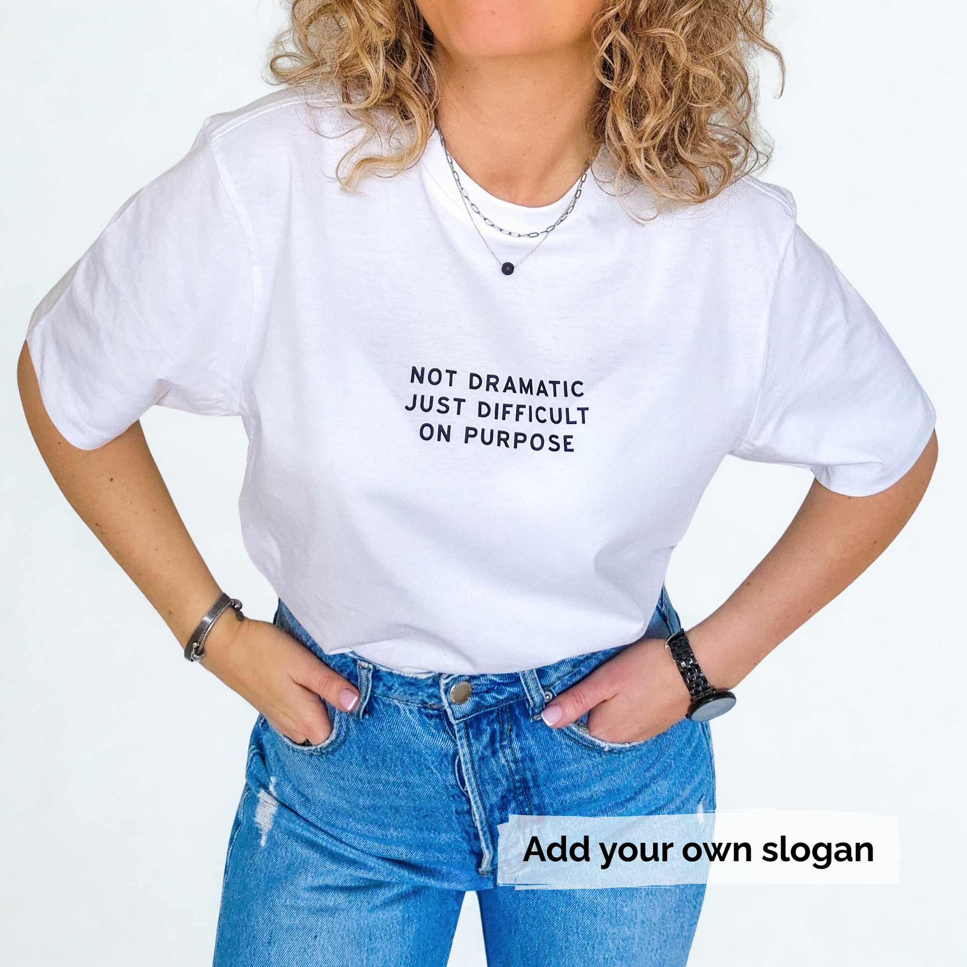 Person wearing a white t-shirt with a printed slogan 'Not dramatic just difficult on purpose' and blue jeans on a light grey background