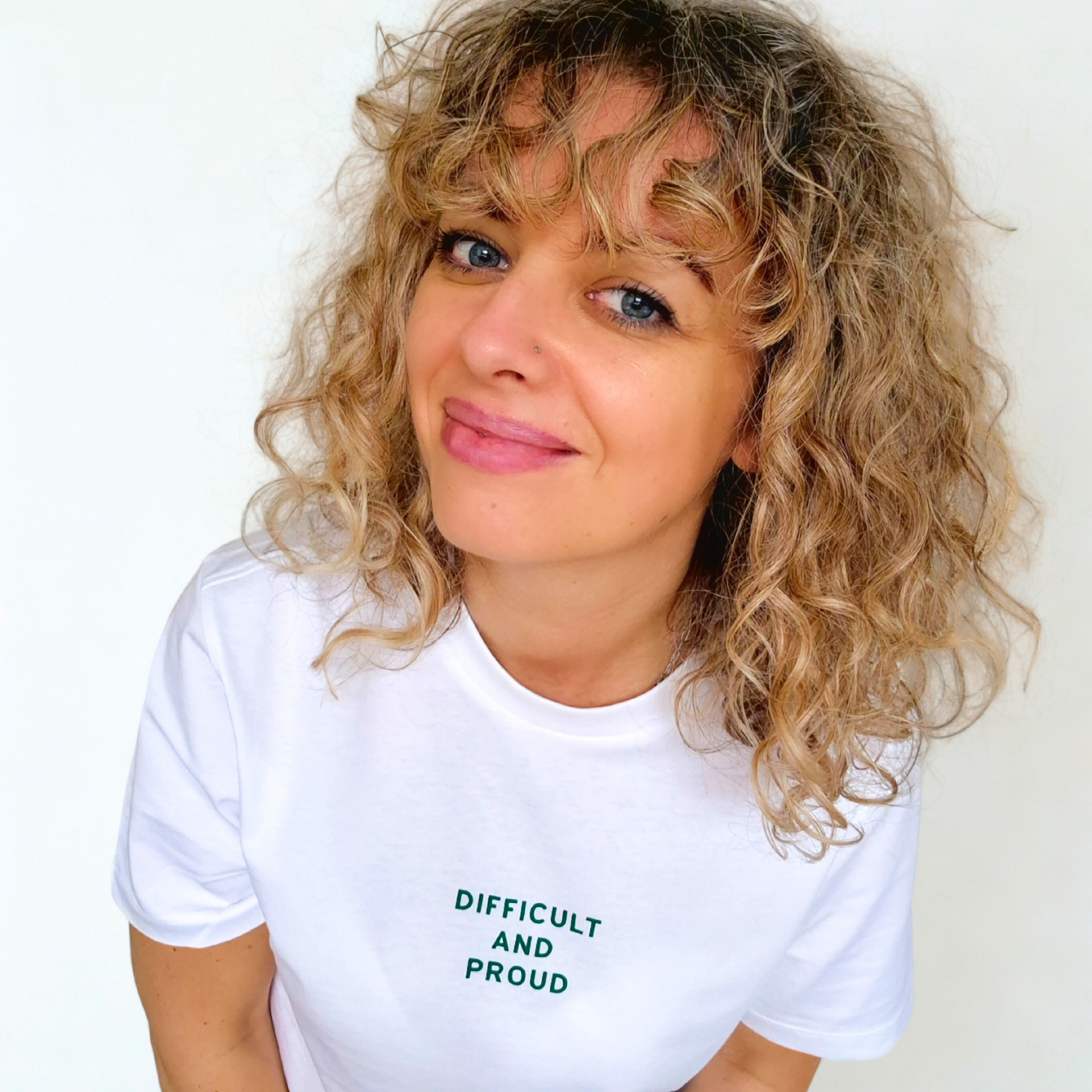 Woman wearing a white t-shirt with 'DIFFICULT AND PROUD' text on a plain background