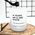 White candle with text 'Mr & Mrs' and personalised message on a wooden stand against a grid background