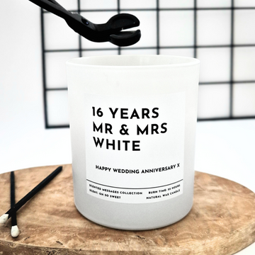 White candle with text 'Mr & Mrs' and personalised message on a wooden stand against a grid background