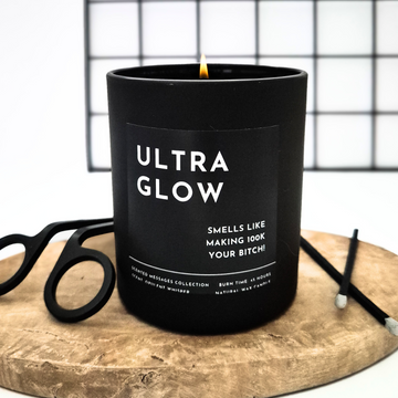 Black candle labelled 'Ultra Glow' with personalised message on a wooden surface.