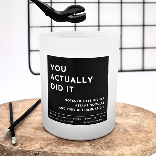 Candle with a label and text 'You actually did it' on a wooden surface