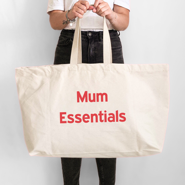 Person holding a beige tote bag with 'Mum Essentials' text on a light gray background