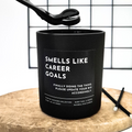 Black candle with text 'Smells like career goals' on a wooden surface and grid background