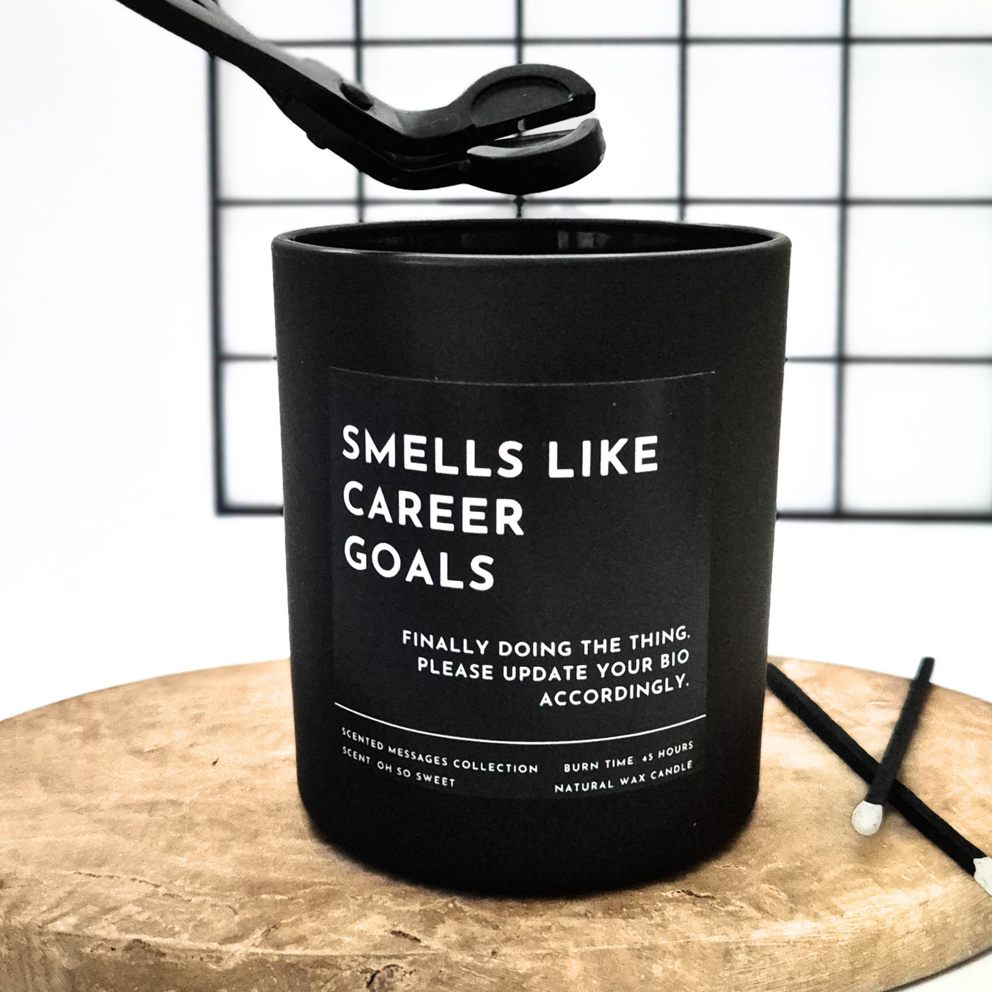 Black candle with text 'Smells like career goals' on a wooden surface and grid background