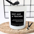 White Candle with a black label and a personalised text in white 'Not just a teacher' and a personalised message underneath 'The person who showed up every single day and made it matter. Thank you Mrs Kent' on a wooden board against a white background