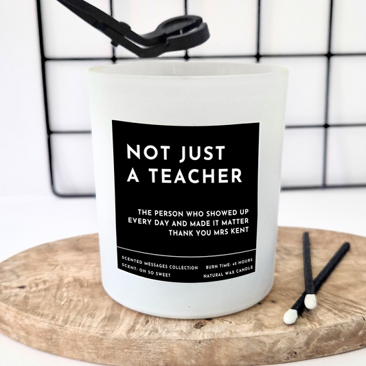 White Candle with a black label and a personalised text in white 'Not just a teacher' and a personalised message underneath 'The person who showed up every single day and made it matter. Thank you Mrs Kent' on a wooden board against a white background