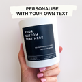 Candle with a label for personalisation held by a hand against a light background