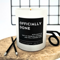 Candle with a humorous label 'Officially done, with hints of not my problem anymore' a wooden board with scissors in the background
