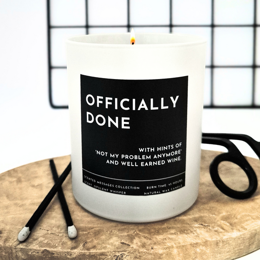 Candle with a humorous label 'Officially done, with hints of not my problem anymore' a wooden board with scissors in the background