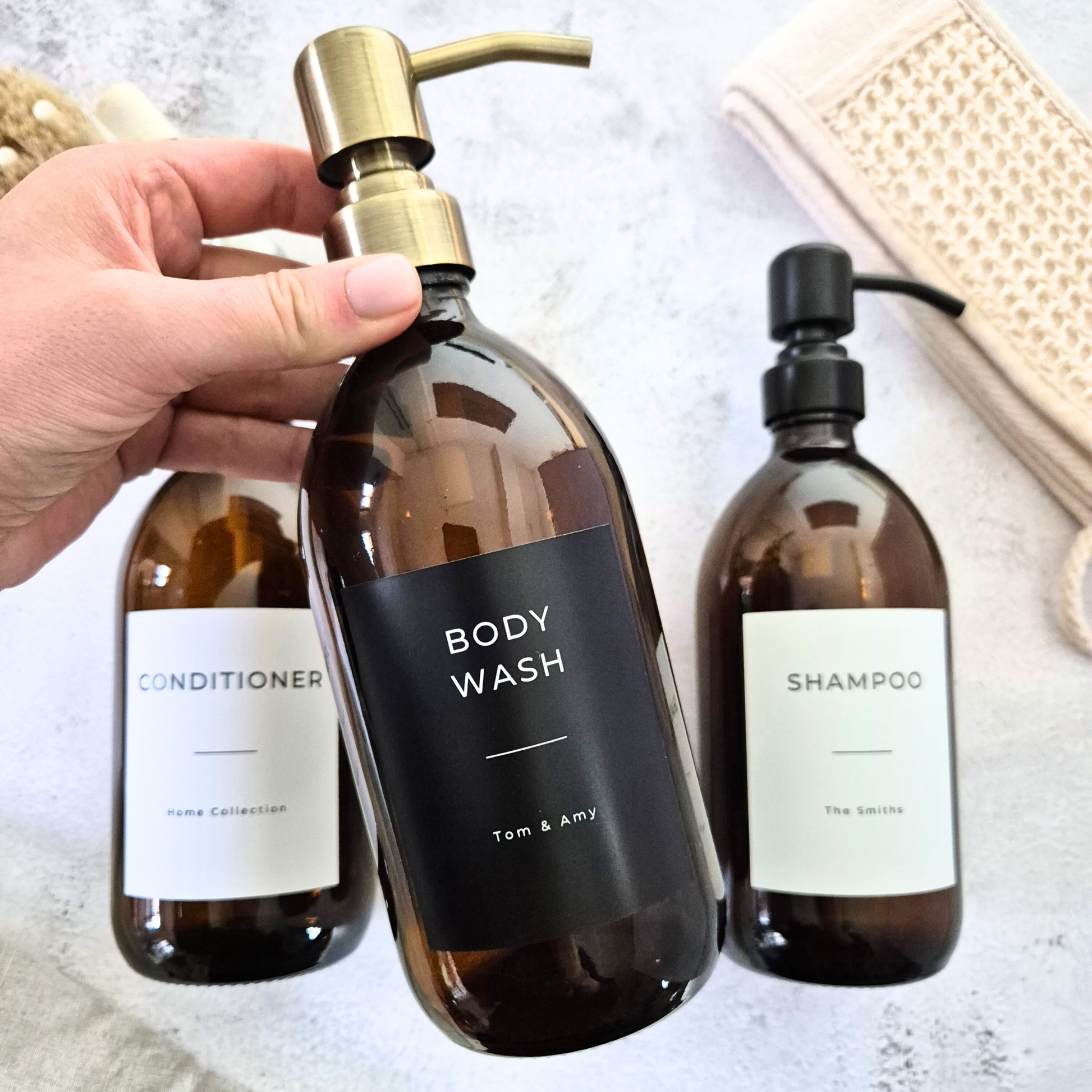 Three brown bottles labeled 'Body Wash', 'Conditioner', and 'Shampoo' on a light surface.