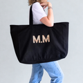 Person holding a black tote bag with 'M.M' in leopard print on a light gray background