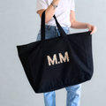 Person holding a black tote bag with 'M.M' initials.