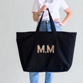 Person holding a black tote bag with 'M.M' in leopard print letters against a plain background