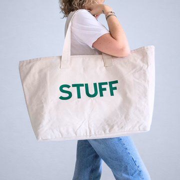 Person holding a beige tote bag with 'STUFF' written in green on a light gray background