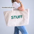 Person holding a large tote bag with 'STUFF' printed on it against a light blue background.